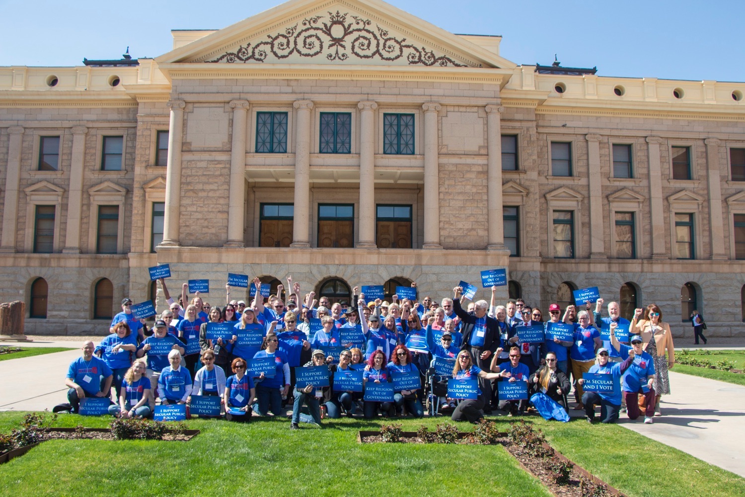 Group of secular supporters wearing blue Secular AZ shirts gather in front of the state capitol to take action toward building the wall between church and state